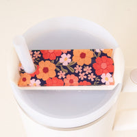 The Darling Effect's Wild About You Navy Tumbler Lid Tag adds a colorful floral touch to your fall tumbler. Shown on a Stanley Quencher 2.0 with orange, red, and pink flowers plus a white straw for stylish hydration.
