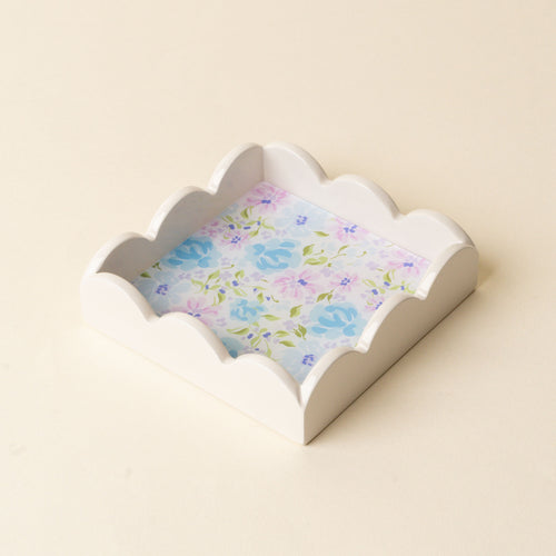 The Secret Garden Blue Scallop Trinket Tray by the-darling-effect features a white, scalloped edge and a blue, purple, and green floral base; perfect as an accessory tray or jewelry organizer on any beige backdrop.