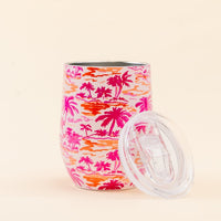 The Darling Effect Paradise Palms Wine Tumbler features a pink and orange palm tree print, triple-wall insulation, and includes a clear spill-resistant lid.