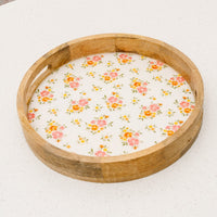 The-darling-effect's Endless Daydream Cream Large Round Wood Enamel Tray features a floral-patterned base with pink, orange, and green accents. Food-safe and stylish, it adds charm to any table setting. Placed on a white speckled surface.