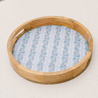 The Petal Parade Blue Large Round Wood Enamel Tray by the-darling-effect features cut-out handles and a blue floral pattern on white, making it a charming choice for stylish serving or display in any setting.