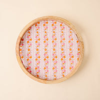 The Petal Parade Pink Large Round Wood Enamel Tray by the-darling-effect features vertical rows of orange and pink florals on a pink base, adding vibrant charm to any setting. Shown on a light beige background.