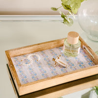 The Petal Parade Blue Rectangle Wood Enamel Tray by the-darling-effect holds a pearl necklace, a pearl-encrusted hair clip, and a perfume bottle with a wooden lid.