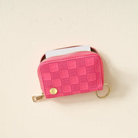 The Darling Effect Hot Pink Check Zip Around Wallet—a compact accessory in a vibrant pink checkered design—features convenient card slots, a gold keyring, and is shown with a card partially sticking out, resting on a light-colored surface.