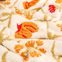 Close-up of The Darling Effect Patchwork Pumpkins Cozy Dreams Luxe Blanket, a soft white microfiber throw featuring textured surface with orange, yellow, and red pumpkin and floral patterns plus green stems.
