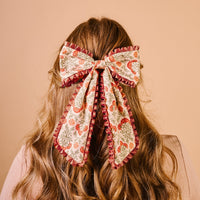 The Darling Effect's Everbloom Dusty Rose Fancy Frills Hair Bow, featuring a ruffle edge and gold barrette clip, is styled at the back of wavy blonde hair.