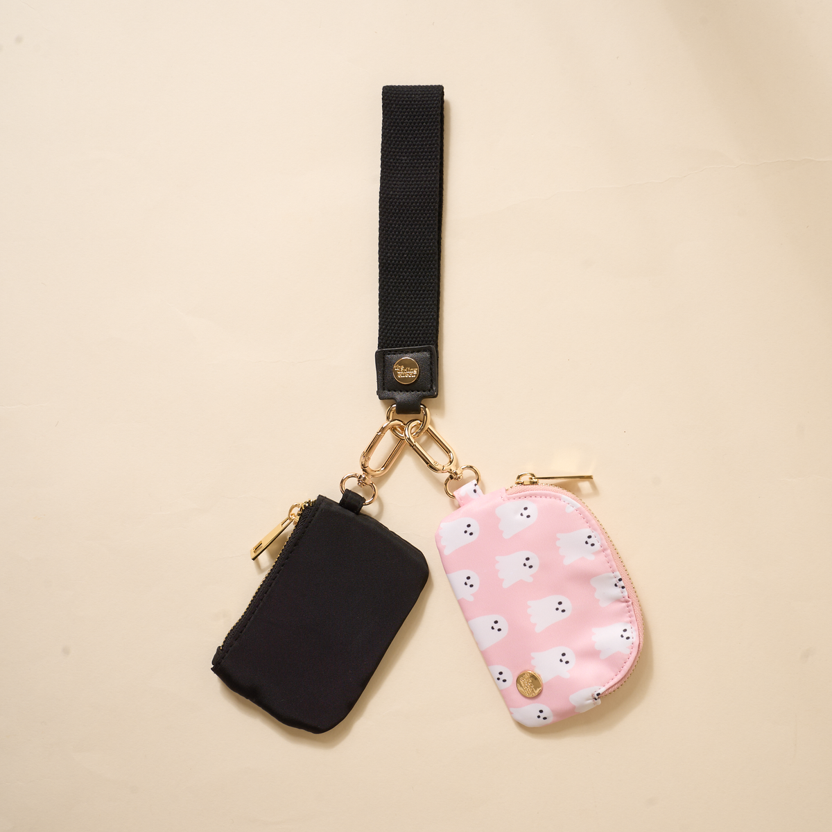 The Darling Effect’s Boo Crew Dynamic Duo Pouch Wristlet features gold hardware and two zippered pouches—one solid black and one pink with white bears—shown hands-free on a light beige background.