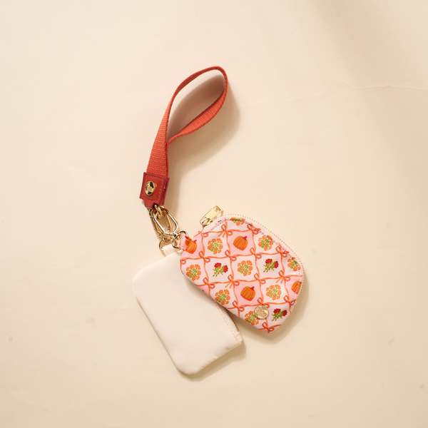 The Darling Effect Patchwork Pumpkins Dynamic Duo Pouch Wristlet features two small zippered pouches—one plain white, one with a colorful pumpkin pattern—attached to a luxe red wristlet with gold clasp for hands-free convenience.