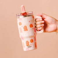 A hand holds The Darling Effect Ghost Party 20 oz Lifestyle Flip Straw Tumbler, a large pink mug with triple-walled insulation and cute pink and orange Halloween ghost and pumpkin designs.