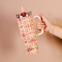 A hand holds The Darling Effect’s Patchwork Pumpkins 40 oz Lifestyle Flip Straw Tumbler, decorated with pumpkins, flowers, and bows on a light peach background and featuring a convenient flip straw lid.