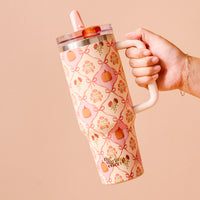 A hand holds The Darling Effect Patchwork Pumpkins 40 oz Lifestyle Flip Straw Tumbler, featuring pink bows, flowers, pumpkins on cream, triple-walled insulation, a handle, clear lid, pink straw, and “Hey There Pumpkin” print on the side.