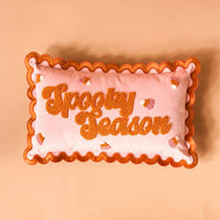 The Darling Effect Spooky Season Scalloped Rectangle Throw Pillow features pink fabric, orange scalloped edges, and textured orange “Spooky Season” lettering with candy corn accents—a playful addition to any sofa or pillow set.