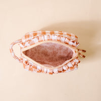 A top view of The Darling Effect Maple Gingham Essentials Quilted Cosmetic Pouch showcases its open, peach and white checkered design with a handle. The makeup bag reveals a pink floral-patterned, wipeable interior lining, set against a light beige background.