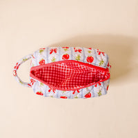 The Darling Effect Oh So Orchard Essentials Quilted Cosmetic Pouch features a blue exterior with red strawberries and green leaves, a red and white checkered interior, zipper, and handle—perfect for organizing makeup essentials on the go.