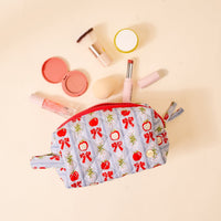The Darling Effect's Oh So Orchard Essentials Quilted Cosmetic Pouch, featuring a red and blue floral pattern, is open with blush, a brush, lipstick, lip gloss, a sponge, and a compact mirror arranged nearby on a light background.