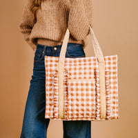 Quilted gingham tote bag carried on shoulder with tan strap and side pockets