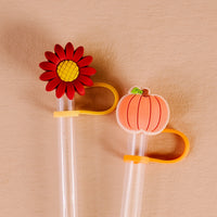 Add a festive autumn flair to your drinks with The Darling Effect’s Petals & Pumpkins Straw Topper Set. This set includes two clear straws, each adorned with a fun silicone topper—one showcasing a vibrant red flower with a yellow center, and the other featuring an orange pumpkin complete with a green stem. Yellow and orange loops accompany both toppers for added charm, making these stylish accessories perfect for keeping your beverages tidy and celebrating the season in style.