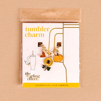 The Darling Effect Happy Harvest Tumbler Charm features a gold chain with sunflower, pumpkin, and heart charms, displayed on a labeled card—perfect for bringing fall vibes to your seasonal tumbler accessories.