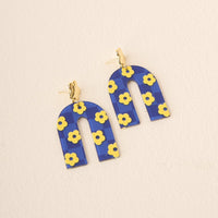 The Darling Effect Navy Yellow Game Day Acrylic Earrings feature arch-shaped acrylic with a blue background, yellow flower pattern, and gold stud accents—ideal for showing school spirit or adding flair to your game day look.