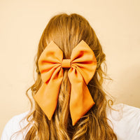 A close-up from behind shows wavy blonde hair styled with The Darling Effect’s Orange Hair Bow—a classic accessory that adds timeless charm to any look.