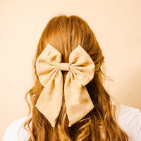 A person's back is shown with long, wavy, light brown hair adorned with The Darling Effect's Tan Hair Bow—a classic satin accessory that adds timeless charm.