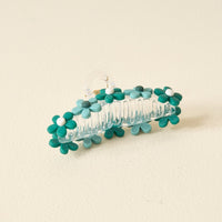 The Darling Effect Green Game Day Daisy Claw Clip features teal and turquoise daisy designs with white centers, shown on a pale cream background—an ideal hair accessory to show off your school spirit on Game Day.