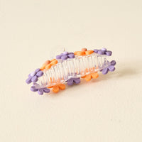 The Darling Effect's Orange Purple Game Day Daisy Claw Clip features clear plastic with purple and orange daisy accents, perfect for highlighting your school colors or adding a playful vibe on Game Day. Photographed on a light, textured background.