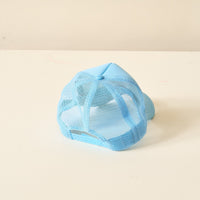 The Darling Effect Light Blue Game Day Trucker Hat is shown upside down on a white surface, with its adjustable strap and mesh back facing the camera, standing out against a neutral background.