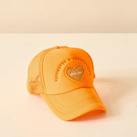 The Darling Effect Orange Game Day Trucker Hat features a heart-shaped foam+day patch and raised embroidered text on the front, perfect for showing team spirit. Displayed against a light beige background.