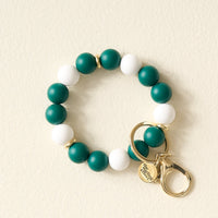 The Darling Effect Green Gameday Hands-Free Keychain Wristlet features alternating green and white beads, gold rings, a lobster clasp, and a round charm engraved with “Simply Southern”—perfect for showing off your school colors.