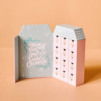 The Darling Effect's Coquette Christmas Ornament Advent Calendar features twelve numbered doors with mini ornaments and a festive “Have Yourself a Merry Little Christmas” message, all displayed on a pastel peach background.