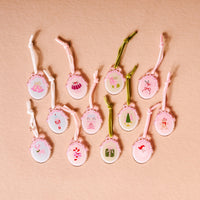 The Darling Effect’s Coquette Christmas Ornament Advent Calendar features twelve pink, scalloped mini ornaments with charming Christmas designs and pastel strings—ideal for decorating artificial trees.