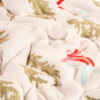 A close-up of The Darling Effect’s Aprés Ski Cozy Dreams Luxe Blanket, an ultra-soft cream polyester microfiber blanket with green, red, and light blue patterns, featuring a cozy textured surface with inviting folds and tufted areas.