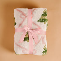 Luxe throw blanket, folded with pale pink ribbon bow and green tree details