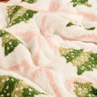 Cozy blanket close-up: fuzzy texture with green tree motifs on pale pink