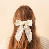 Close-up back view of a person with long brown hair in a half-up ponytail, styled with The Darling Effect's Cream Pearl Hair Bow—an elegant, cream-colored accessory adorned with tiny pearls for a chic look.