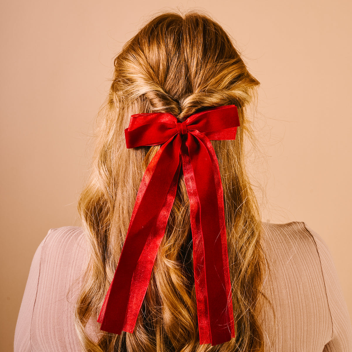 A red velvet layered Red Velvet Luxe Layered Hair Bow by The Darling Effect tied at the back of a woman’s wavy, half-up hairstyle.