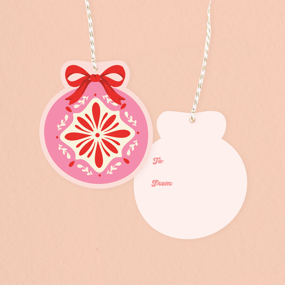 The Darling Effect’s Merry Ornaments Gift Tag Set includes two ornament-shaped tags on white and gold string—one with a red bow and floral design, the other blank with "To:" and "From:" in pink script. Ideal for holiday gifting.