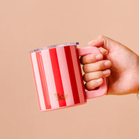 A hand holds a Peppermint Stripes 14 oz Insulated Mug, featuring pink and red stripes and a clear lid.