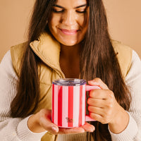 A person holding a pink and red striped Peppermint Stripes 14 oz Insulated Mug with a clear lid.