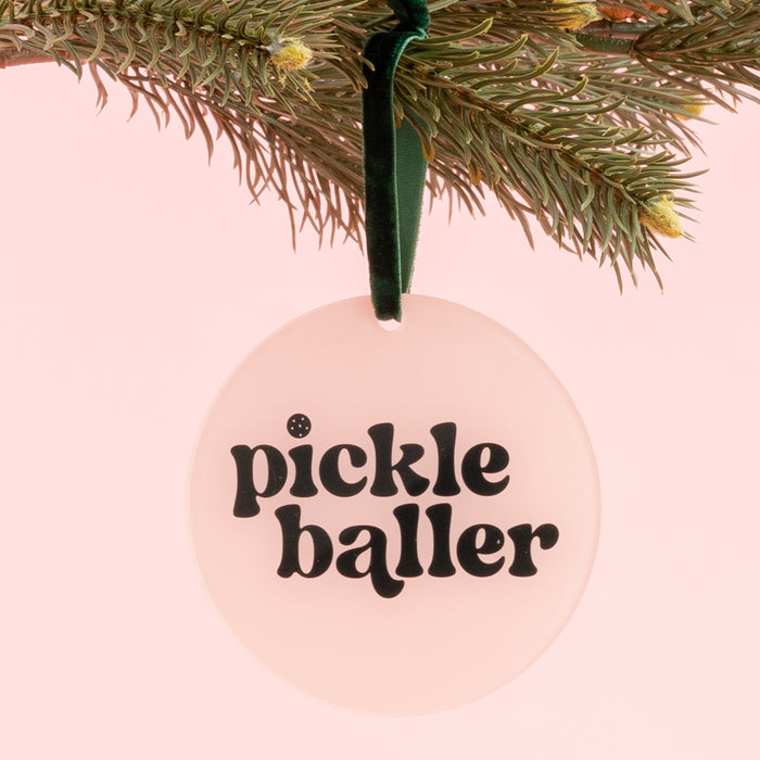 Add a playful touch to your holiday décor with The Darling Effect’s Holiday Tree Ornament - Pickleballer, featuring bold black “pickle baller” text on a light pink background. This round acrylic ornament hangs from a pine branch with a green ribbon and makes the perfect festive statement for pickleball fans this season.