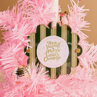 The Darling Effect's Evergreen Stripes Scalloped Round Picture Frame Ornament hangs on a pink artificial Christmas tree, featuring green and gold accents and the phrase “Have Yourself a Merry Little Christmas,” with a pink ornament nearby.