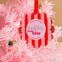 The Darling Effect's Peppermint Stripes Scalloped Round Picture Frame Ornament, featuring pink and white stripes and "kinda naughty, kinda nice" text, hangs on a pink Christmas tree with silver accents. Fits a 2-inch photo.
