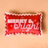 The Darling Effect Merry & Bright Scalloped Rectangle Throw Pillow is a red rectangular decorative pillow with pink scalloped edges, textured pink MERRY & bright lettering, and white star icons.