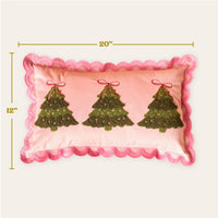 The Darling Effect's Twinkling Trees Scalloped Rectangle Throw Pillow adds a cozy, festive touch with pink fabric, embroidered green Christmas trees, red bows, and pink ornaments. Measures 12" x 20".