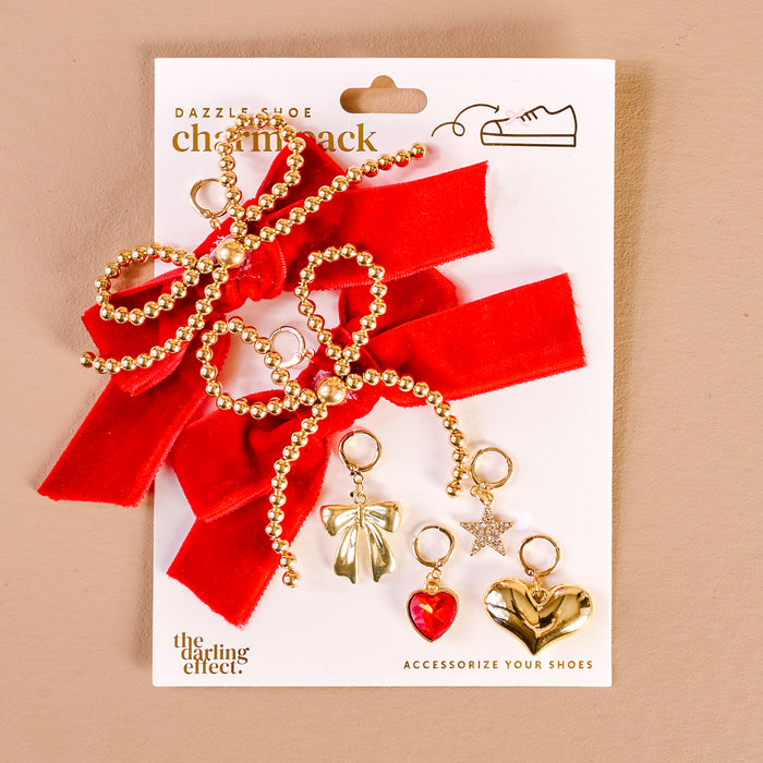 The Darling Effect's 'Tis the Season Dazzle Shoe Charm Pack includes two red velvet bows with gold bead loops and four metallic sneaker charms—a silver bow, red heart, gold star, and gold heart—on a branded backing card.