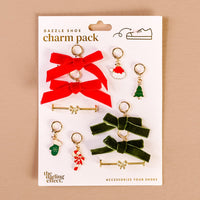 The Darling Effect’s Very Merry Dazzle Shoe Charm Pack features red and green velvet bows, a Santa face, Christmas tree, stocking, candy cane, and gold shoe bars on a white card.