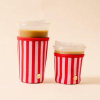 Two iced coffee cups with clear lids, each fitted with The Darling Effect Peppermint Stripes Sip Savvy Drink Sleeve, are placed side by side against a light beige background.