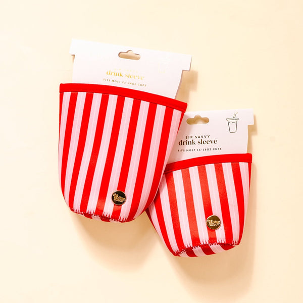 Two Peppermint Stripes Sip Savvy Drink Sleeves by The Darling Effect, each featuring festive red and white stripes with a gold logo, are displayed against a light background. The packaging notes that these sleeves fit most 16–18 oz cups. Crafted from durable neoprene, these holiday drink sleeves are ideal for keeping your favorite seasonal beverages warm in style.