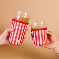 Two hands holding iced drinks in clear cups with The Darling Effect Peppermint Stripes Sip Savvy Drink Sleeve against a beige background.